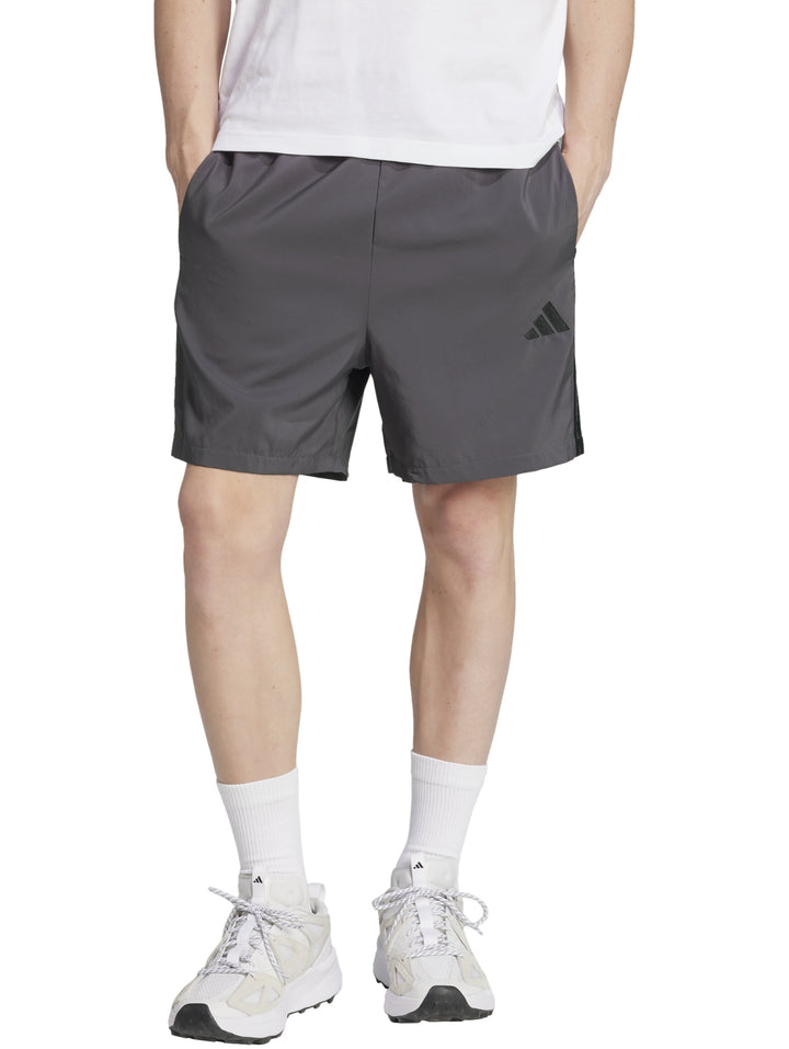 Hombre vistiendo pantalones cortos deportivos Adidas en color gris con logo negro lateral.