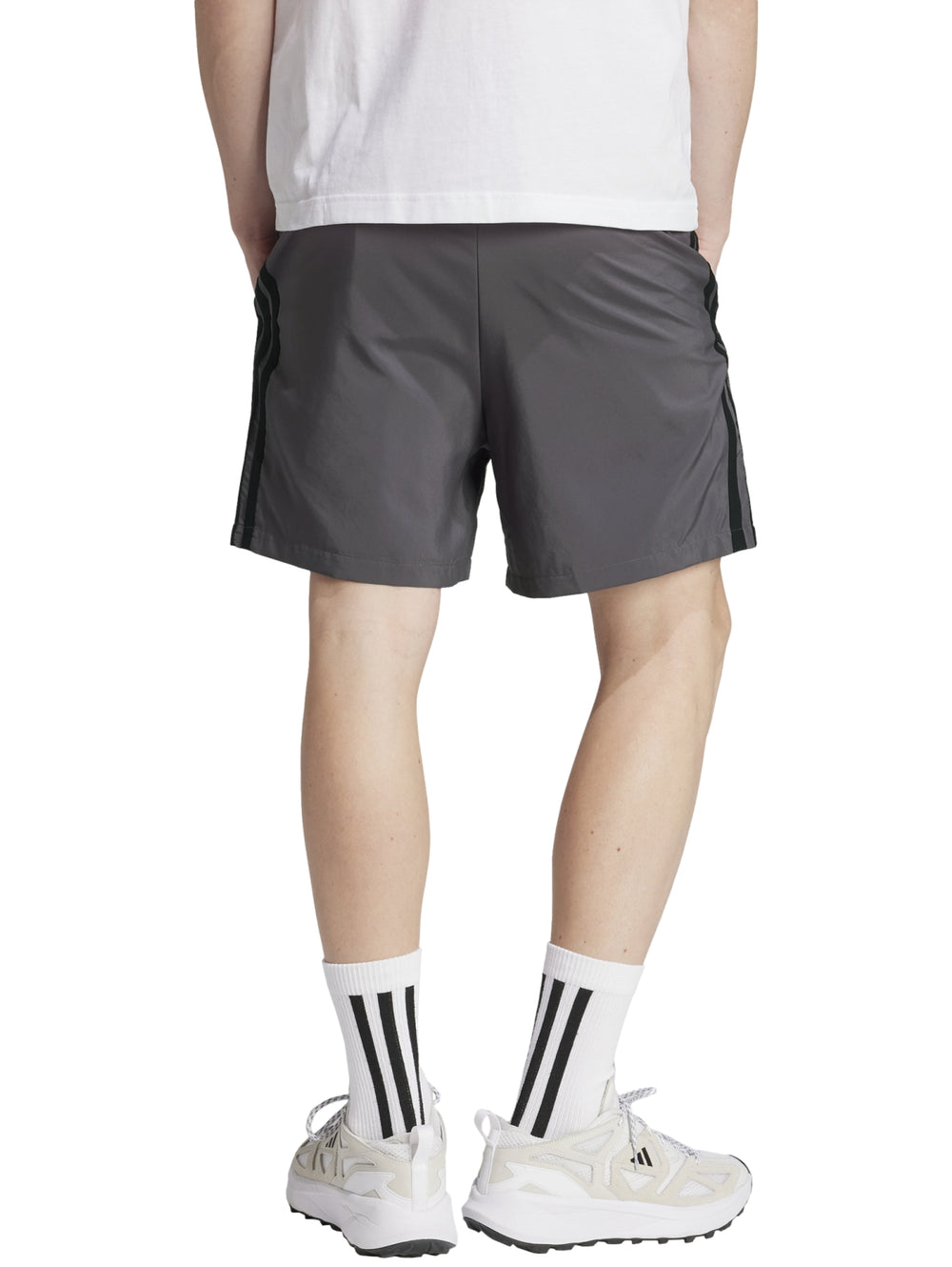 Hombre vistiendo pantalones cortos deportivos Adidas en color gris con logo negro lateral.