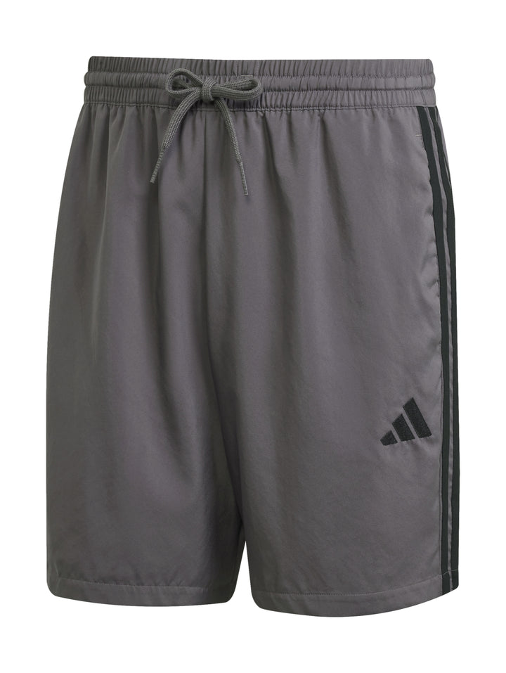 Hombre vistiendo pantalones cortos deportivos Adidas en color gris con logo negro lateral.