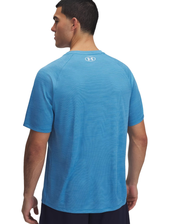 Hombre vistiendo una camiseta deportiva Under Armour de color azul ether blue con textura y logo blanco en el pecho.