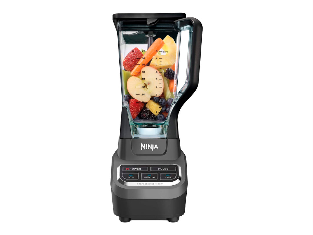 Licuadora profesional Ninja negra con vaso de vidrio transparente lleno de frutas frescas troceadas.