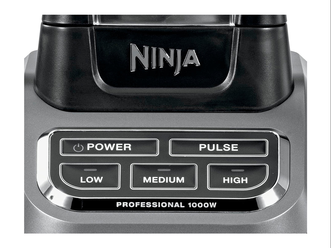 Licuadora profesional Ninja negra con vaso de vidrio transparente lleno de frutas frescas troceadas.
