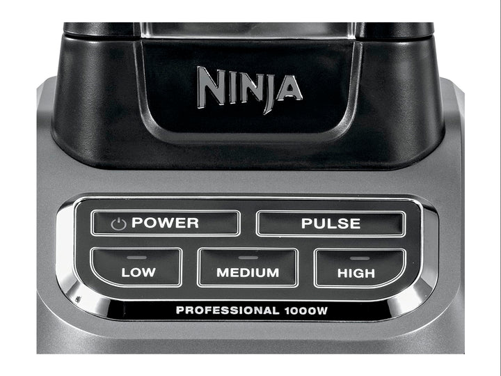 Licuadora profesional Ninja negra con vaso de vidrio transparente lleno de frutas frescas troceadas.