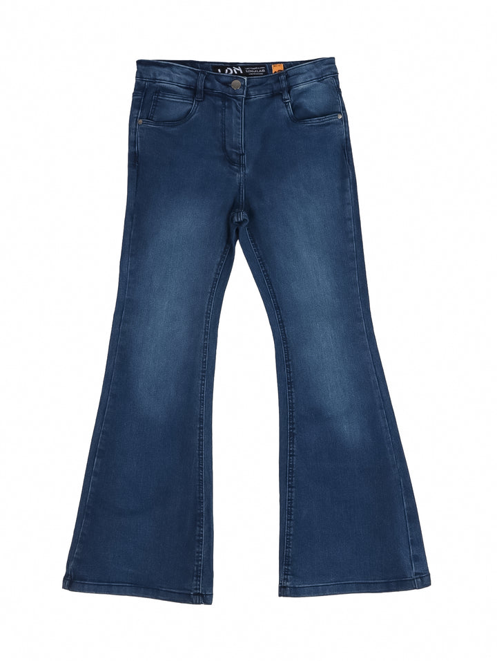 Niña vistiendo pantalón de mezclilla azul oscuro de corte acampanado y playera blanca.