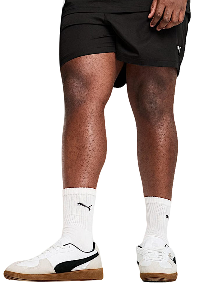 Hombre vistiendo shorts deportivos PUMA de color negro, calcetines blancos y tenis blancos.