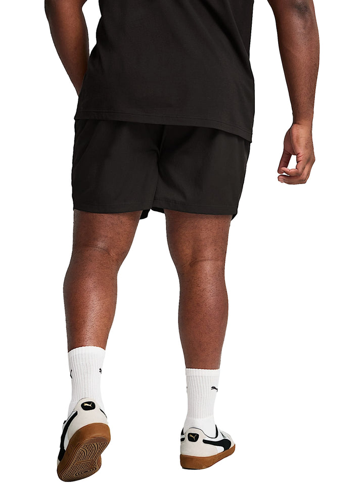 Hombre vistiendo shorts deportivos PUMA de color negro, calcetines blancos y tenis blancos.