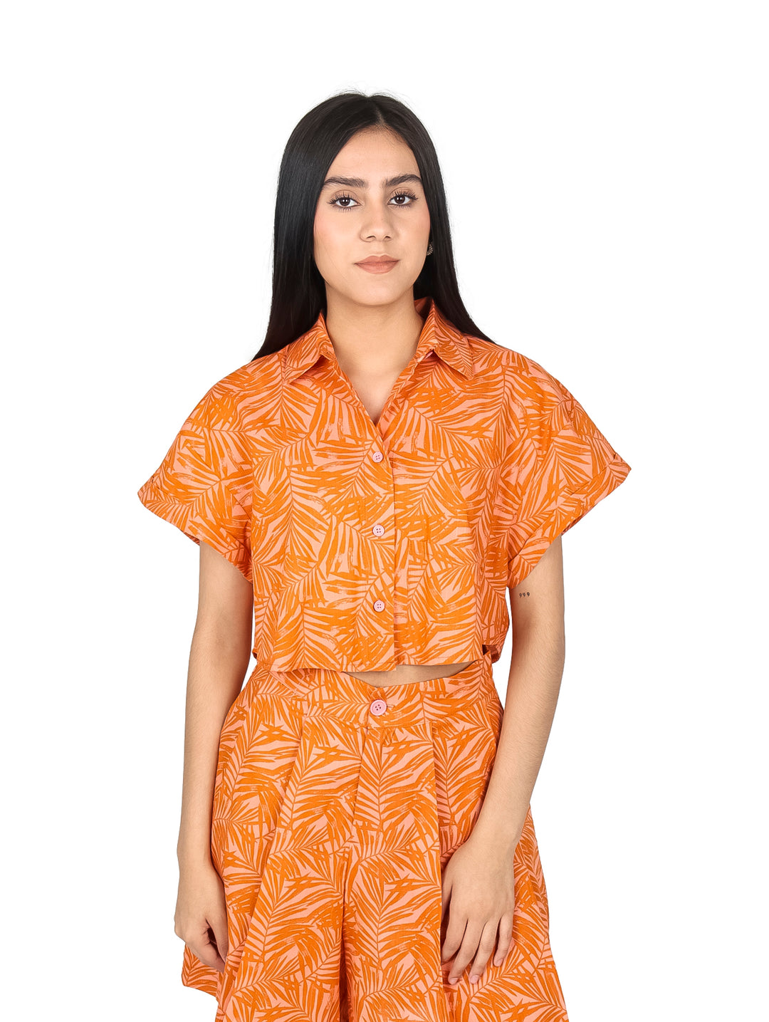 Mujer vistiendo un top corto color naranja con estampado de hojas y botones frontales.