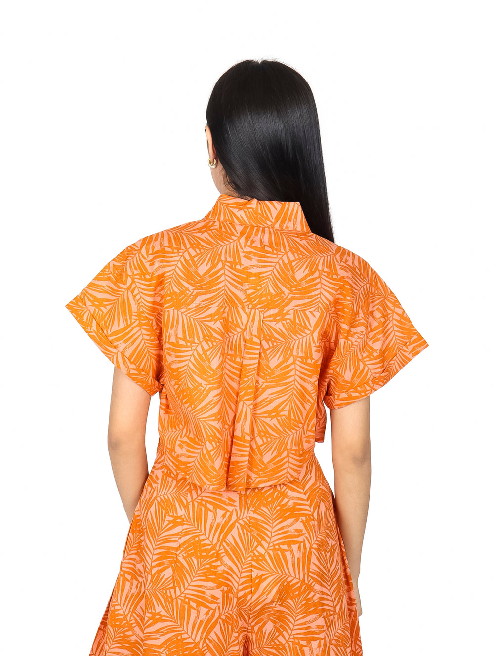 Mujer vistiendo un top corto color naranja con estampado de hojas y botones frontales.