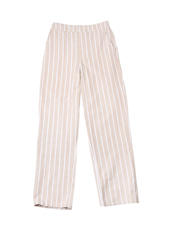 Mujer vistiendo un pantalón beige con rayas blancas verticales y una camiseta blanca.