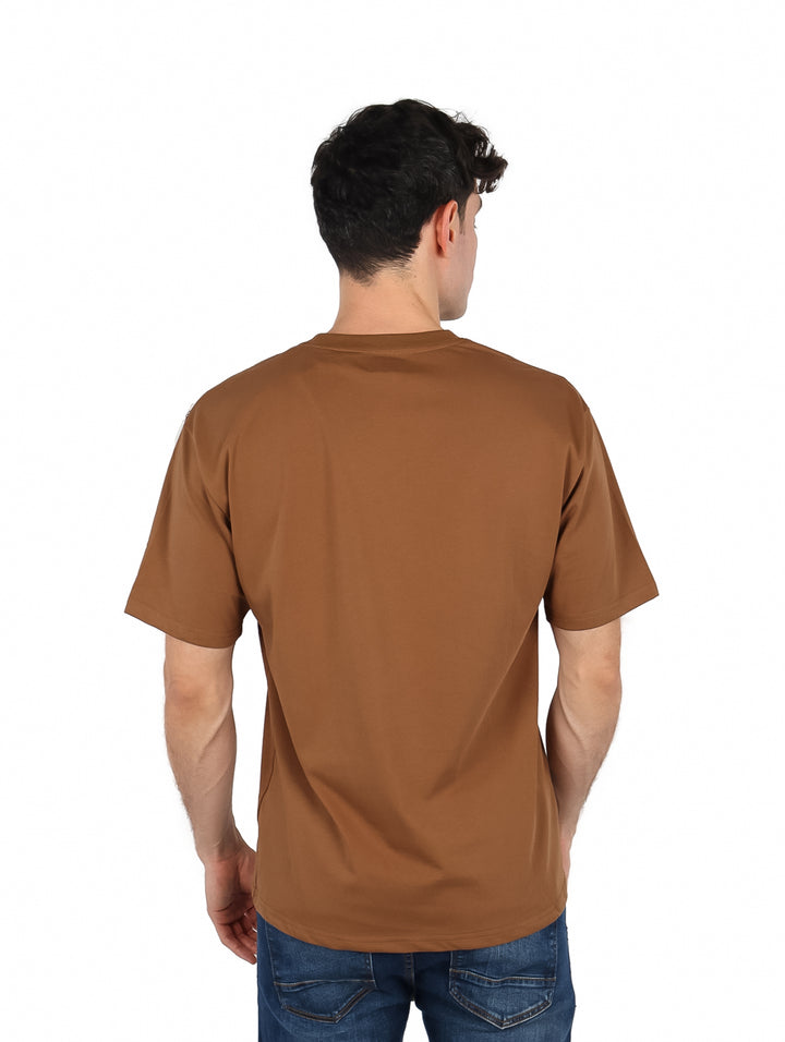 Hombre vistiendo una playera oversize de color café con cuello redondo y manga corta.
