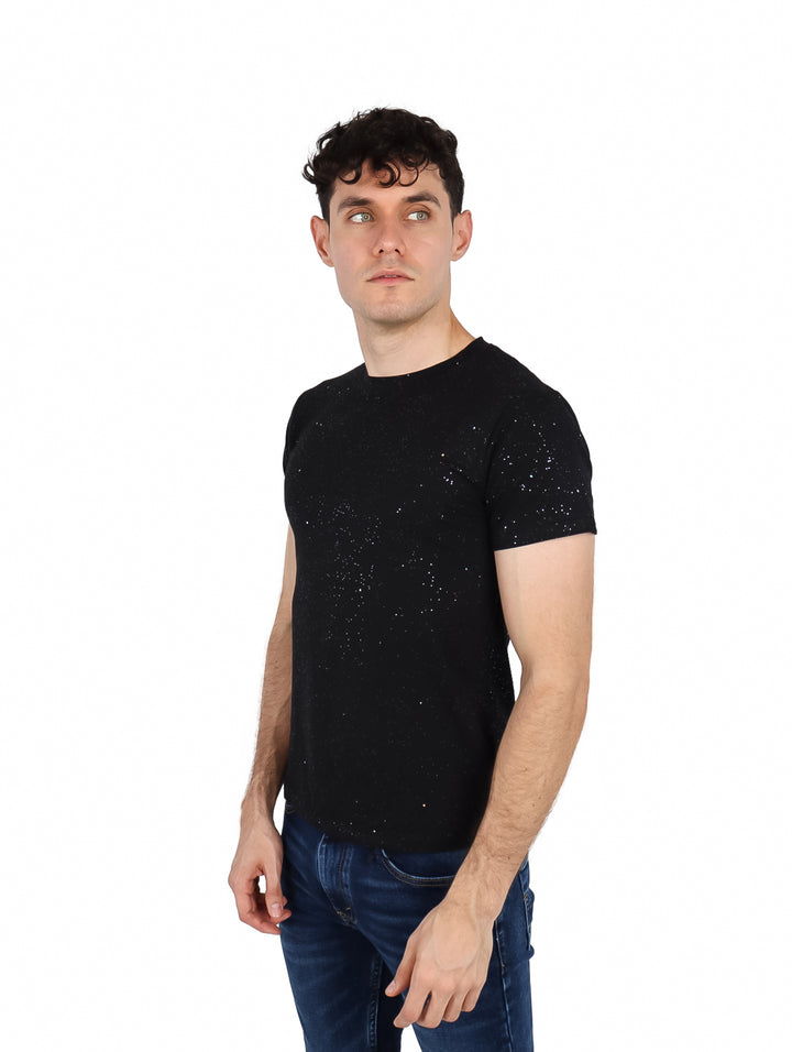 Hombre vistiendo playera negra de manga corta con efecto de salpicaduras blancas y cuello redondo.