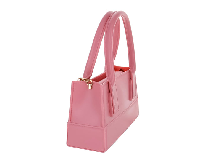 Bolso de mano color rosa pastel con diseño rectangular y asas cortas sobre fondo blanco.