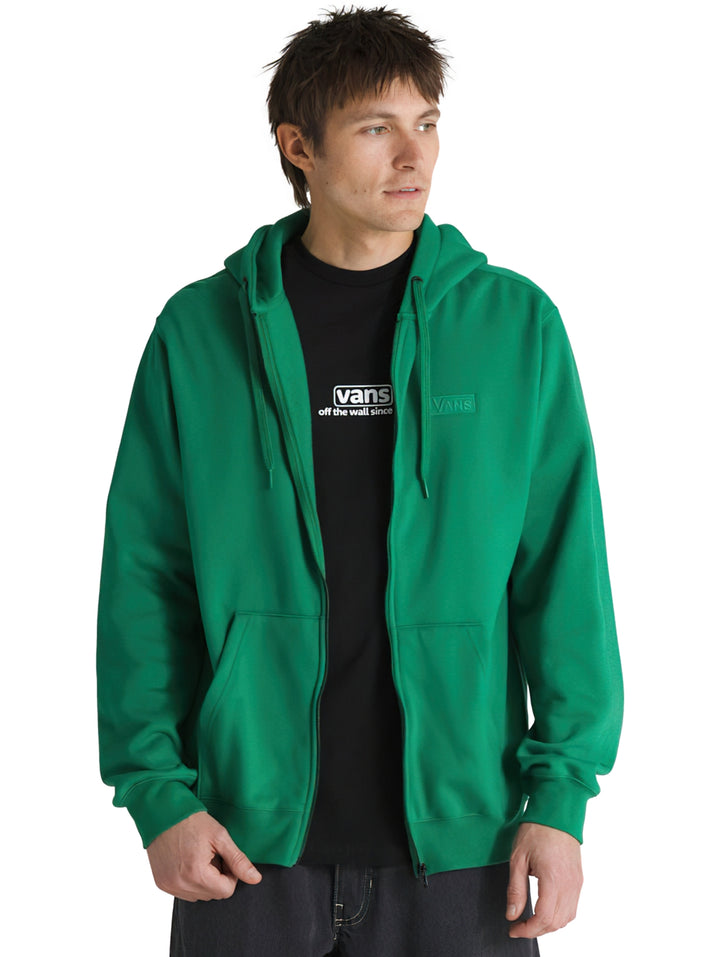 Hombre usando sudadera verde con capucha y cierre frontal de la marca Vans.