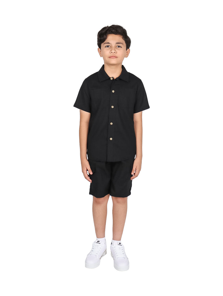 Niño vistiendo un conjunto de camisa y short color negro con tenis blancos.