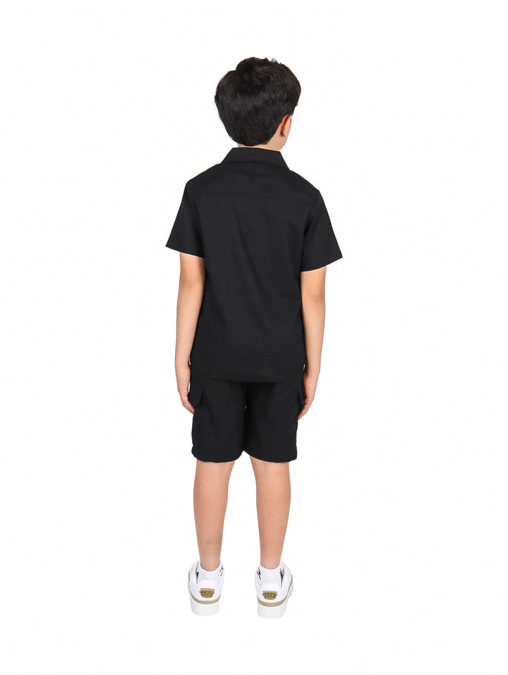Niño vistiendo un conjunto de camisa y short color negro con tenis blancos.
