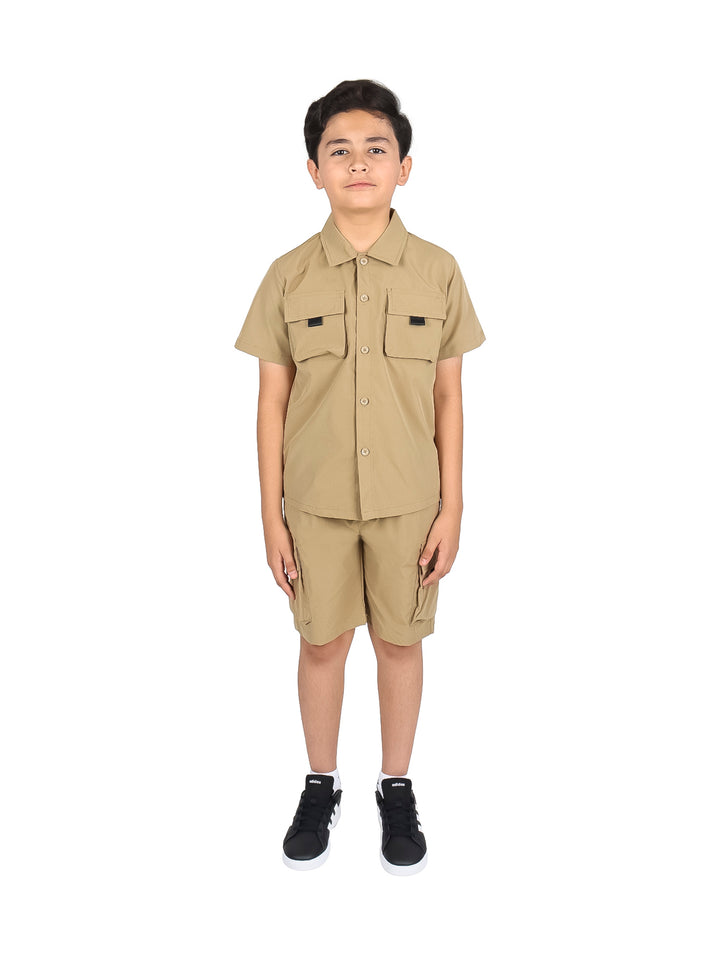 Niño vistiendo un conjunto casual de camisa y shorts en color khaki con tenis negros.