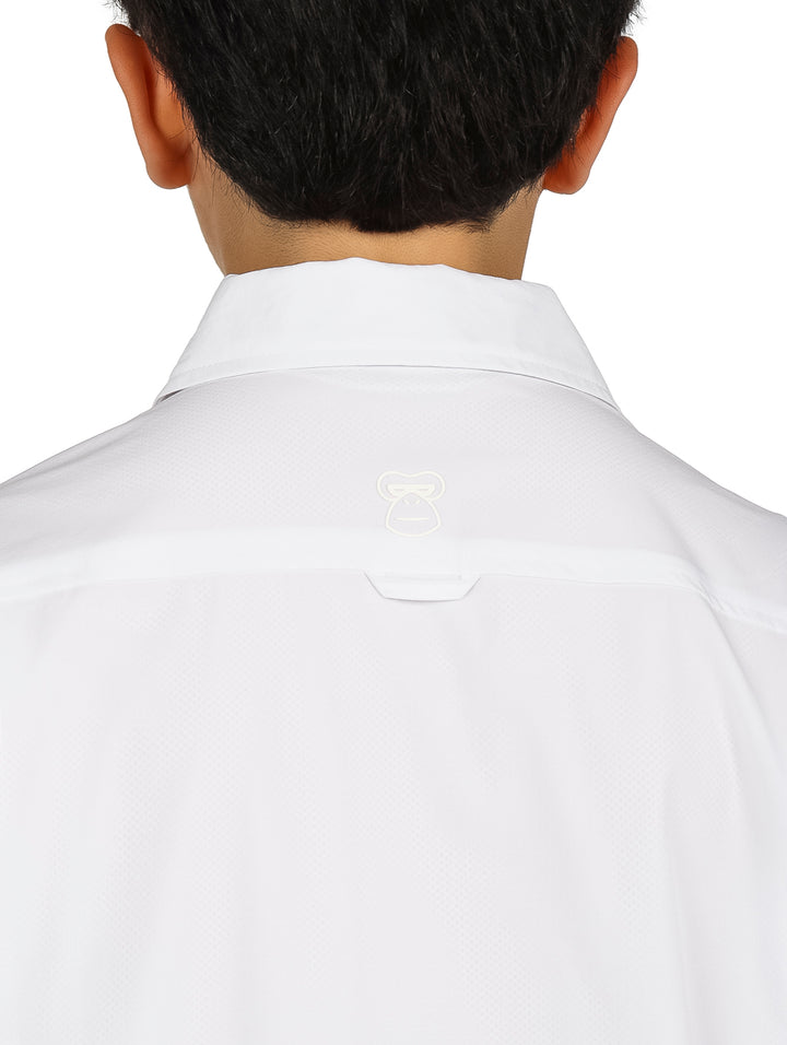 Niño con camisa blanca de manga corta y pantalones negros sobre fondo blanco.