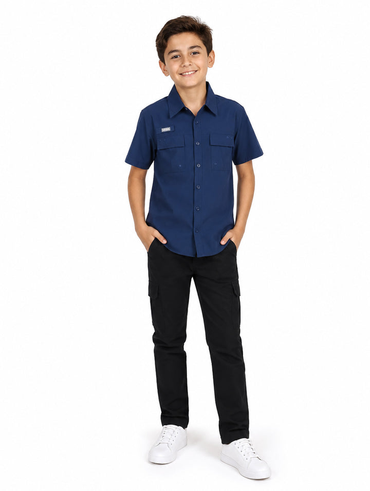 Niño usando camisa azul navy de manga corta con bolsillos frontales y pantalones negros.