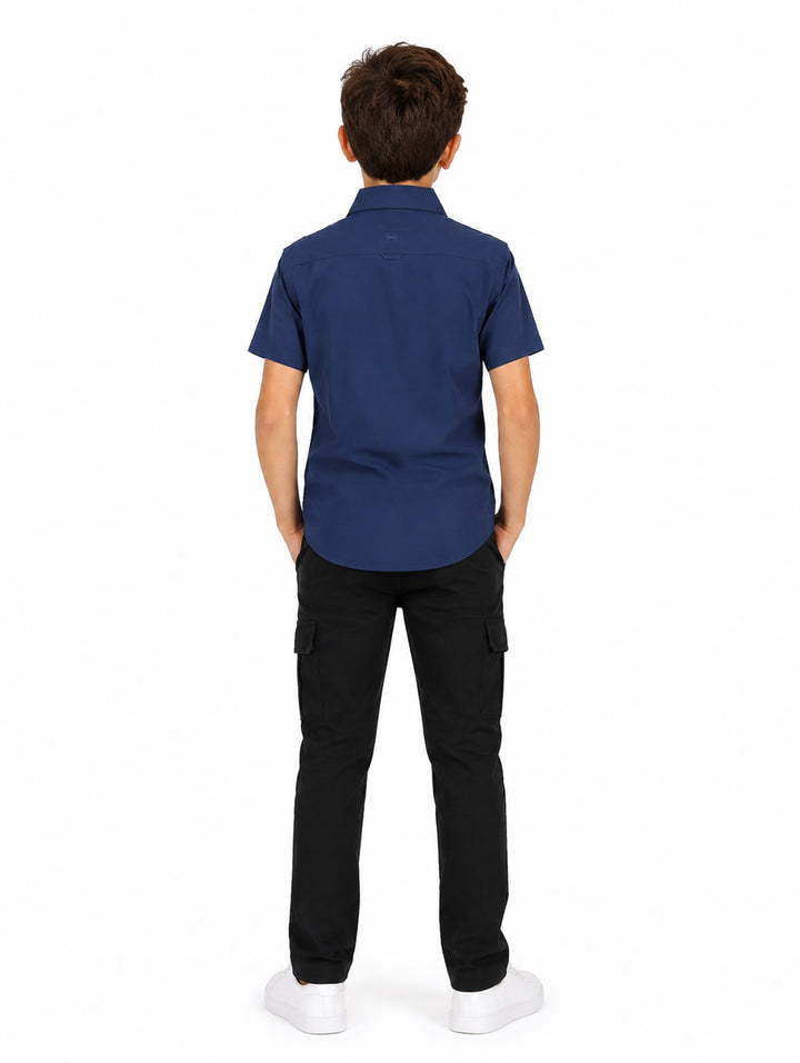 Niño usando camisa azul navy de manga corta con bolsillos frontales y pantalones negros.