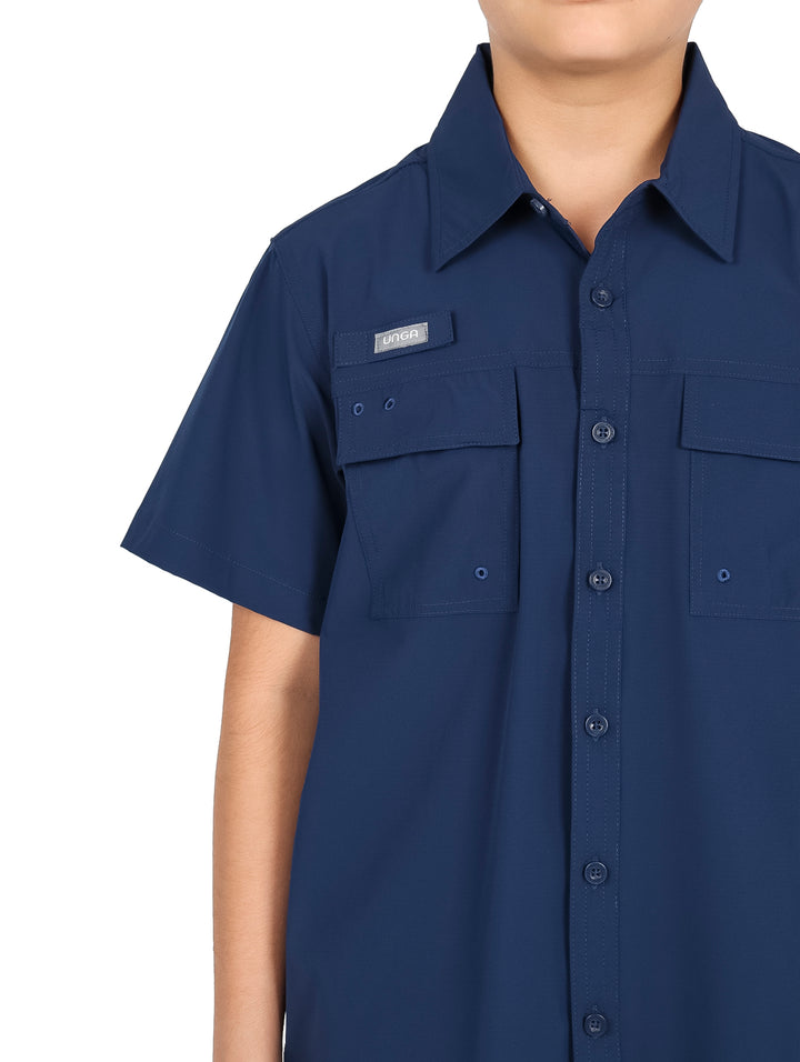 Niño usando camisa azul navy de manga corta con bolsillos frontales y pantalones negros.