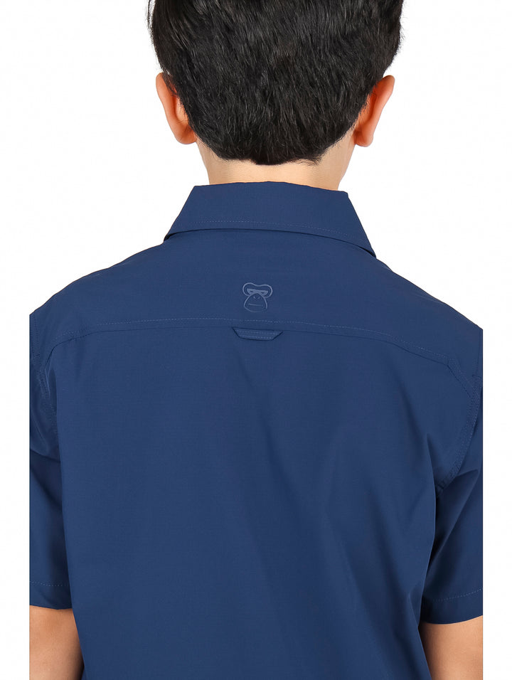 Niño usando camisa azul navy de manga corta con bolsillos frontales y pantalones negros.