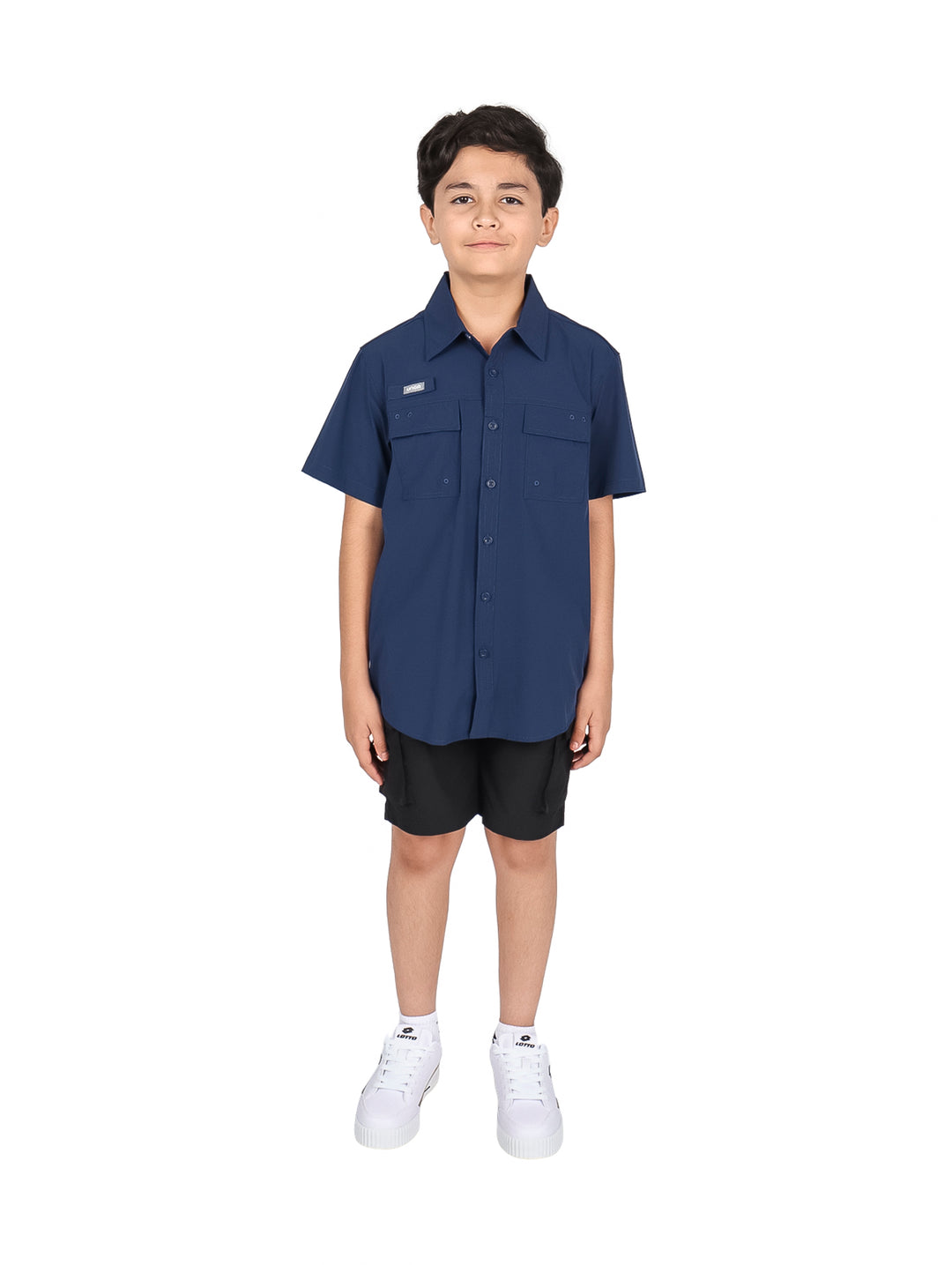 Niño usando camisa azul navy de manga corta con bolsillos frontales y pantalones negros.