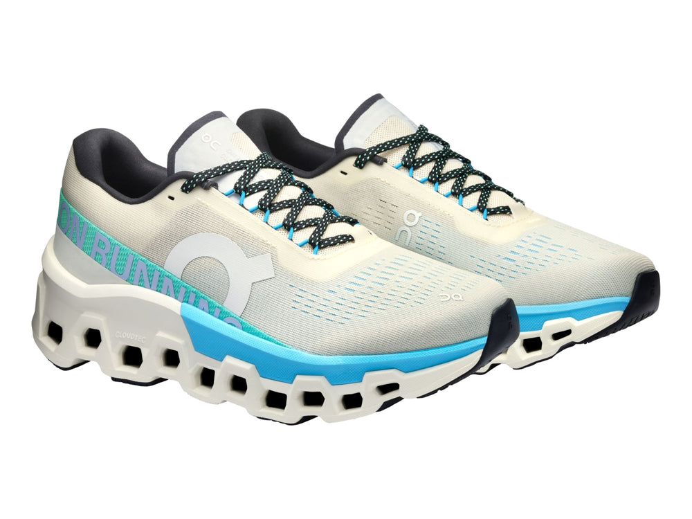 Tenis deportivos On Cloudmonster 2 en color crema con detalles en azul y suela blanca estructural.