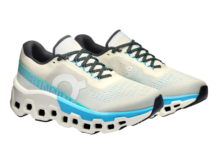 Tenis deportivos On Cloudmonster 2 en color crema con detalles en azul y suela blanca estructural.