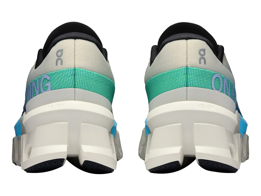 Tenis deportivos On Cloudmonster 2 en color crema con detalles en azul y suela blanca estructural.
