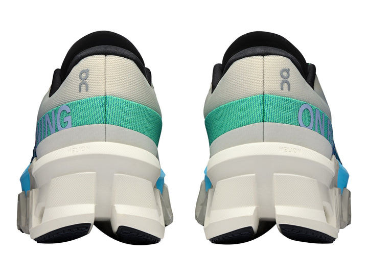Tenis deportivos On Cloudmonster 2 en color crema con detalles en azul y suela blanca estructural.