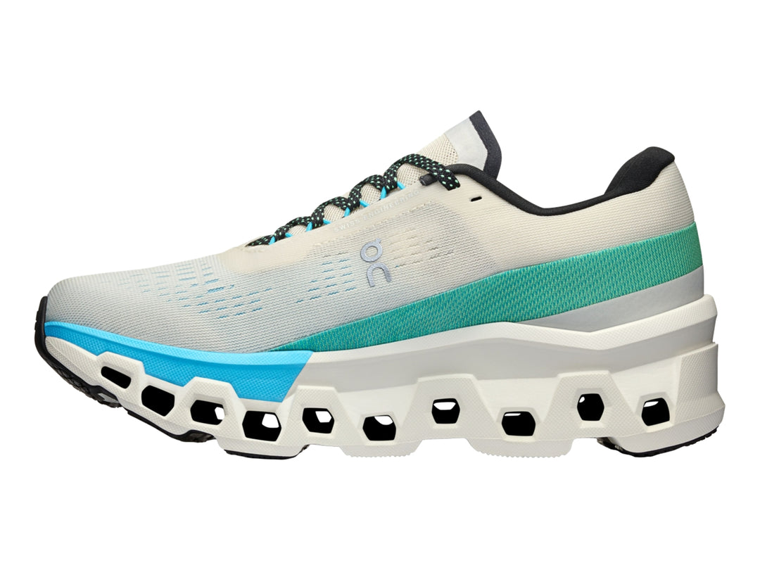 Tenis deportivos On Cloudmonster 2 en color crema con detalles en azul y suela blanca estructural.