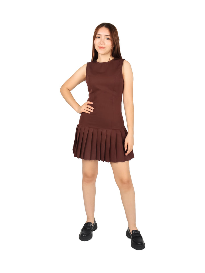 Mujer vistiendo un vestido corto color marrón, sin mangas y con falda plisada.