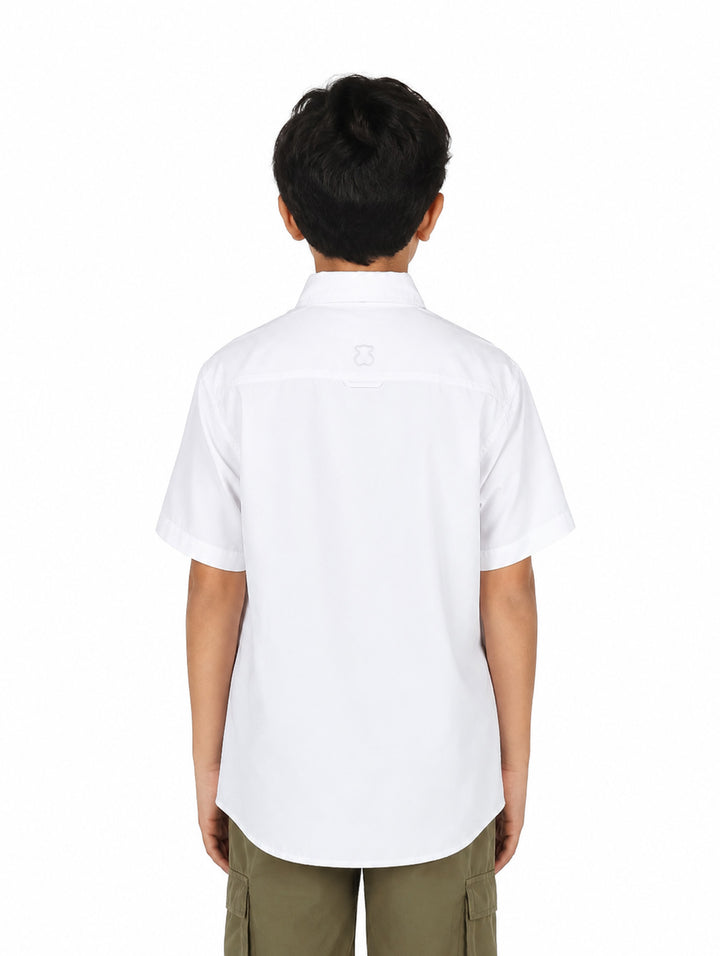 Niño vistiendo una camisa outdoor de color blanco con manga corta y dos bolsillos frontales.