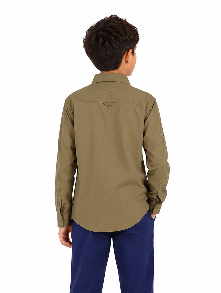 Niño vistiendo una camisa de manga larga color verde militar con dos bolsillos frontales y cuello.