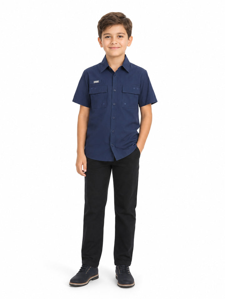 Niño vistiendo una camisa casual color navy de manga corta con bolsillos frontales y pantalones negros.