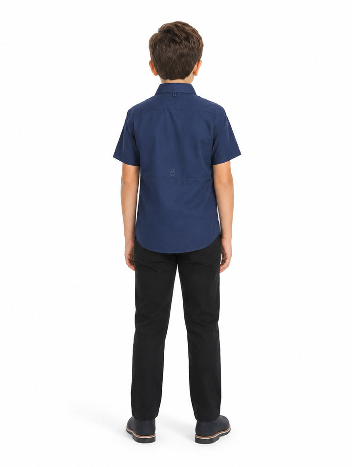 Niño vistiendo una camisa casual color navy de manga corta con bolsillos frontales y pantalones negros.