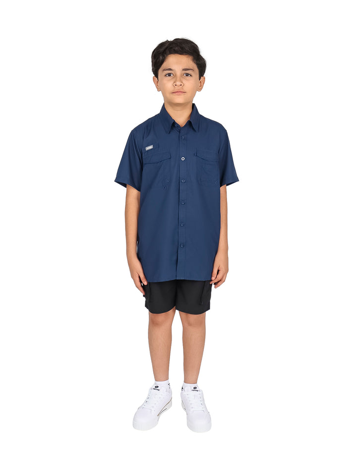 Niño vistiendo una camisa casual color navy de manga corta con bolsillos frontales y pantalones negros.