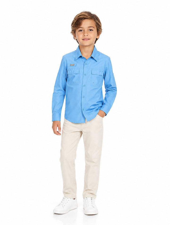 Niño modelando una camisa azul de manga larga, pantalones beige y tenis blancos sobre fondo blanco.