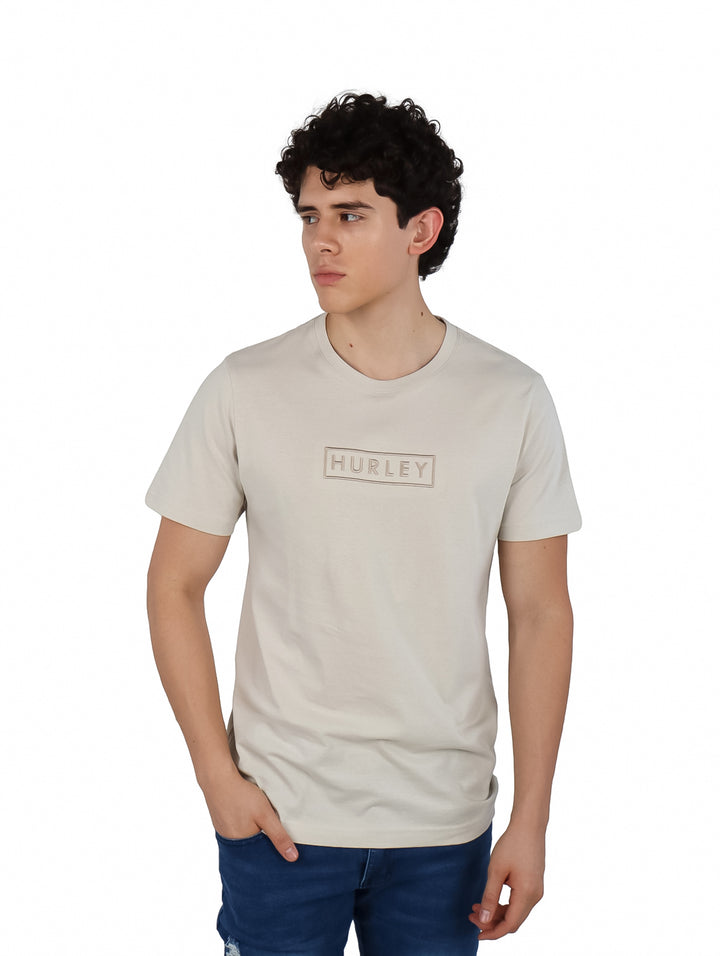 Hombre vistiendo una camiseta Hurley de color hueso con logotipo bordado en el pecho y manga corta.