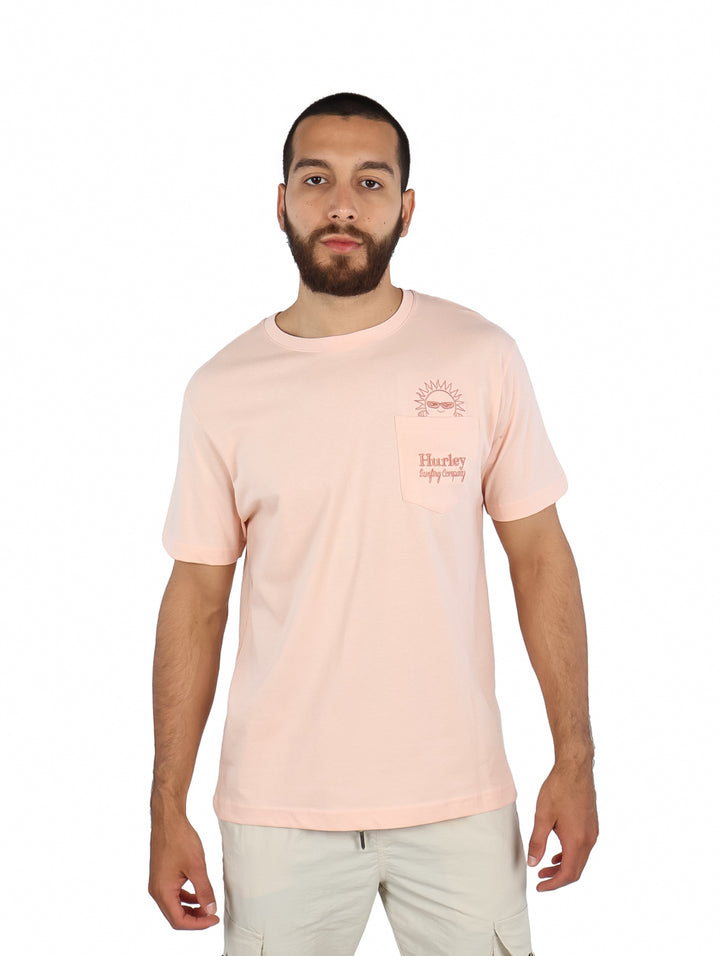 Hombre vistiendo una camiseta de manga corta color rosa claro con un pequeño bolsillo frontal y gráfico.