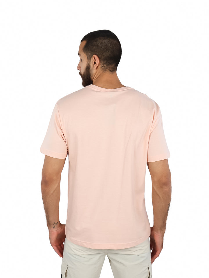 Hombre vistiendo una camiseta de manga corta color rosa claro con un pequeño bolsillo frontal y gráfico.