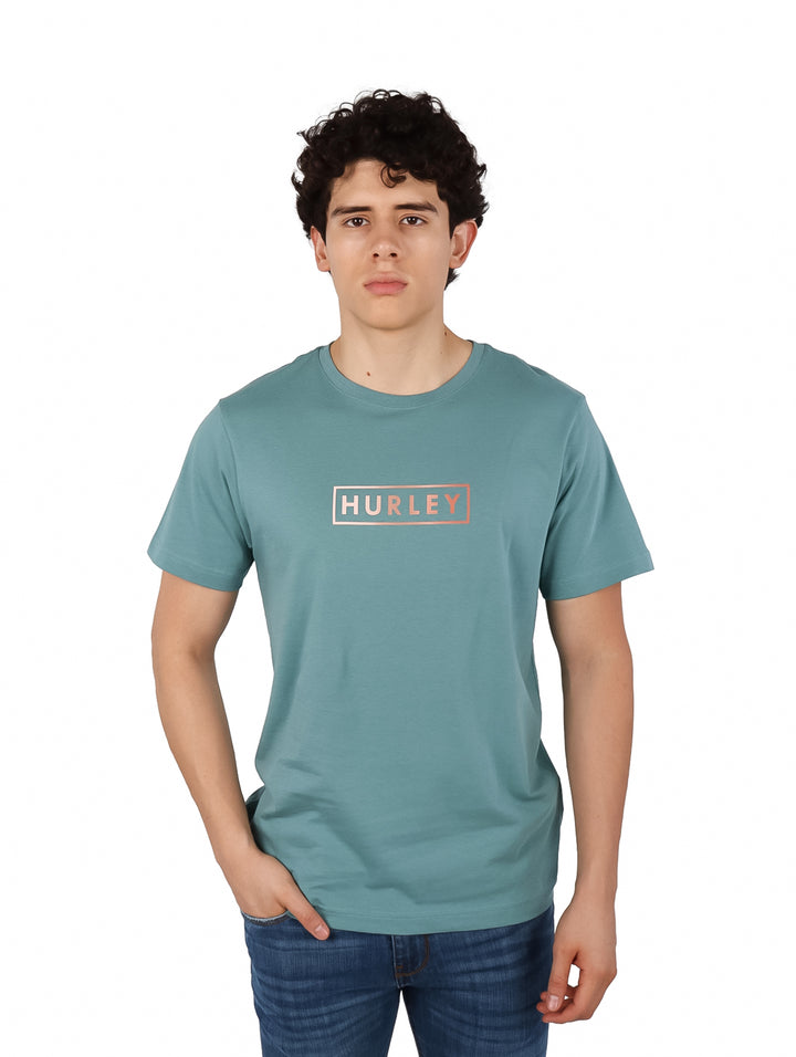 Hombre vistiendo camiseta de manga corta color verde azulado con logo de Hurley en el pecho.