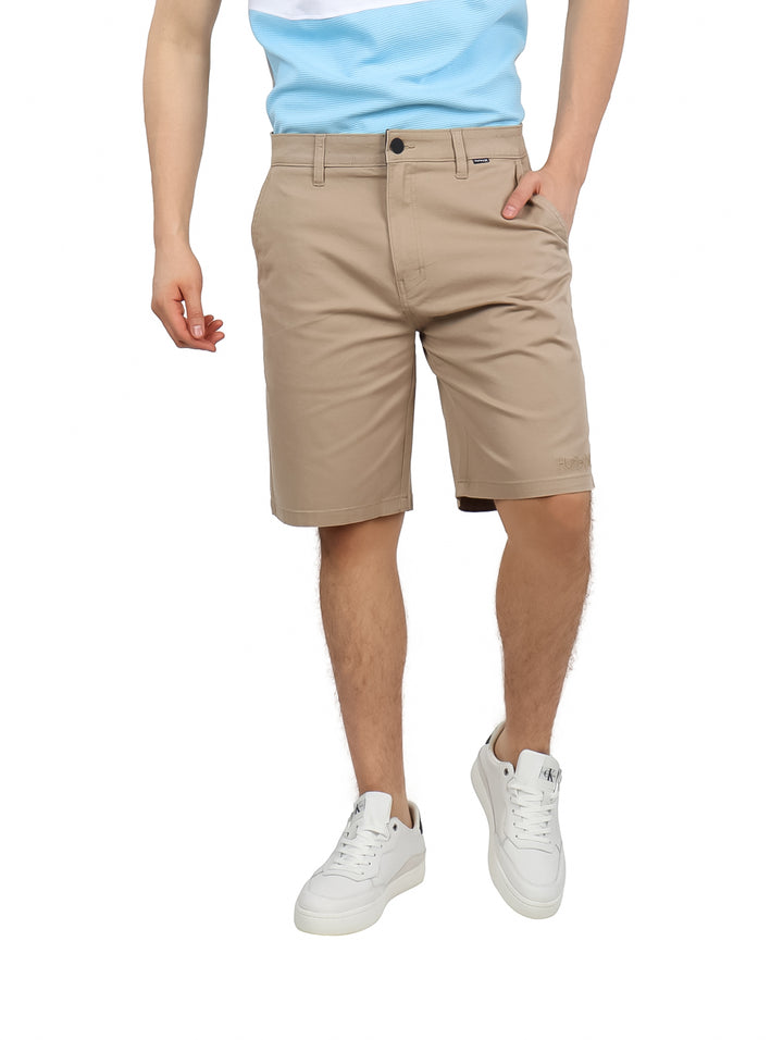 Hombre vistiendo pantalones cortos Hurley de color khaki estilo clásico twill con tenis blancos.