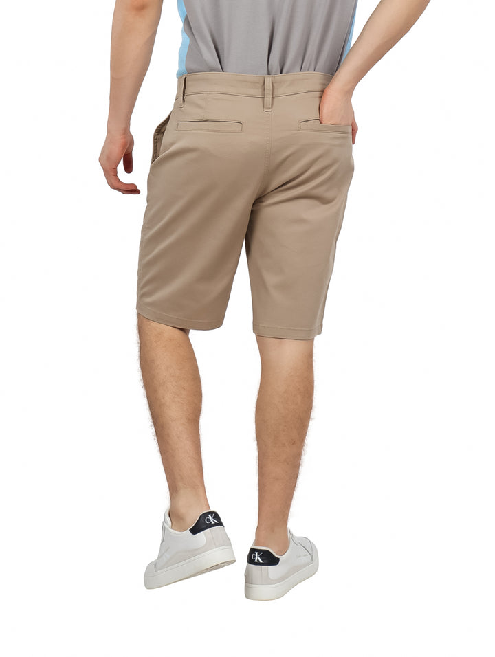 Hombre vistiendo pantalones cortos Hurley de color khaki estilo clásico twill con tenis blancos.