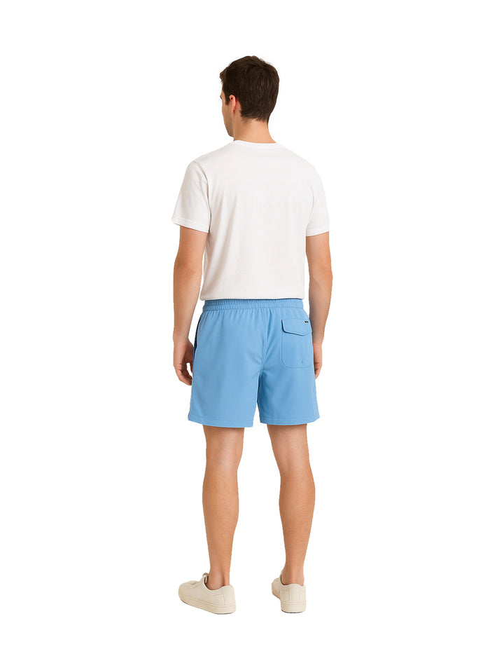 Hombre vistiendo shorts de natación Hurley color azul claro con camiseta blanca y tenis blancos.