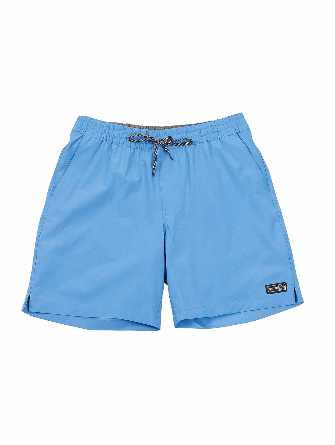 Hombre vistiendo shorts de natación Hurley color azul claro con camiseta blanca y tenis blancos.