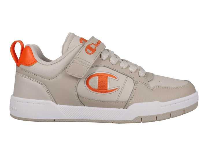Tenis Champion color beige con detalles en naranja, suela blanca y cierre de agujetas con correa de velcro.
