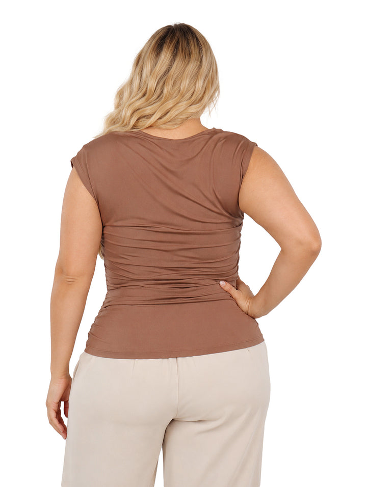 Mujer vistiendo blusa color marrón con cuello asimétrico y diseño drapeado.