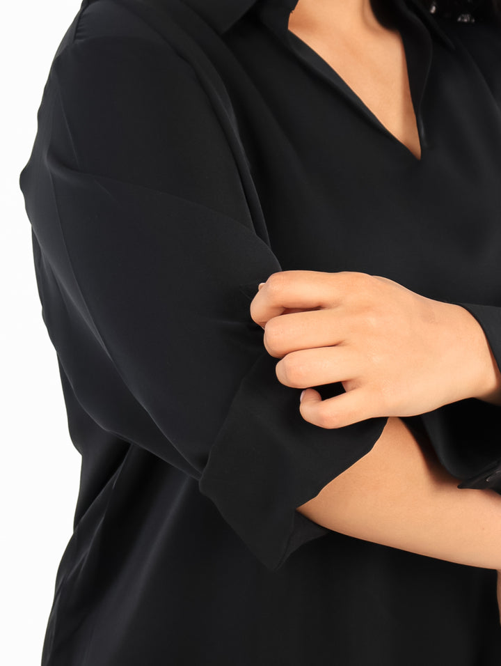 Mujer vistiendo una camisa negra de manga larga con cuello y botones, estilo casual.