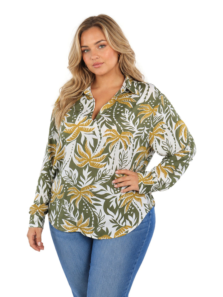 Mujer vistiendo camisa de botones con estampado de hojas tropicales en colores verde, mostaza y blanco.